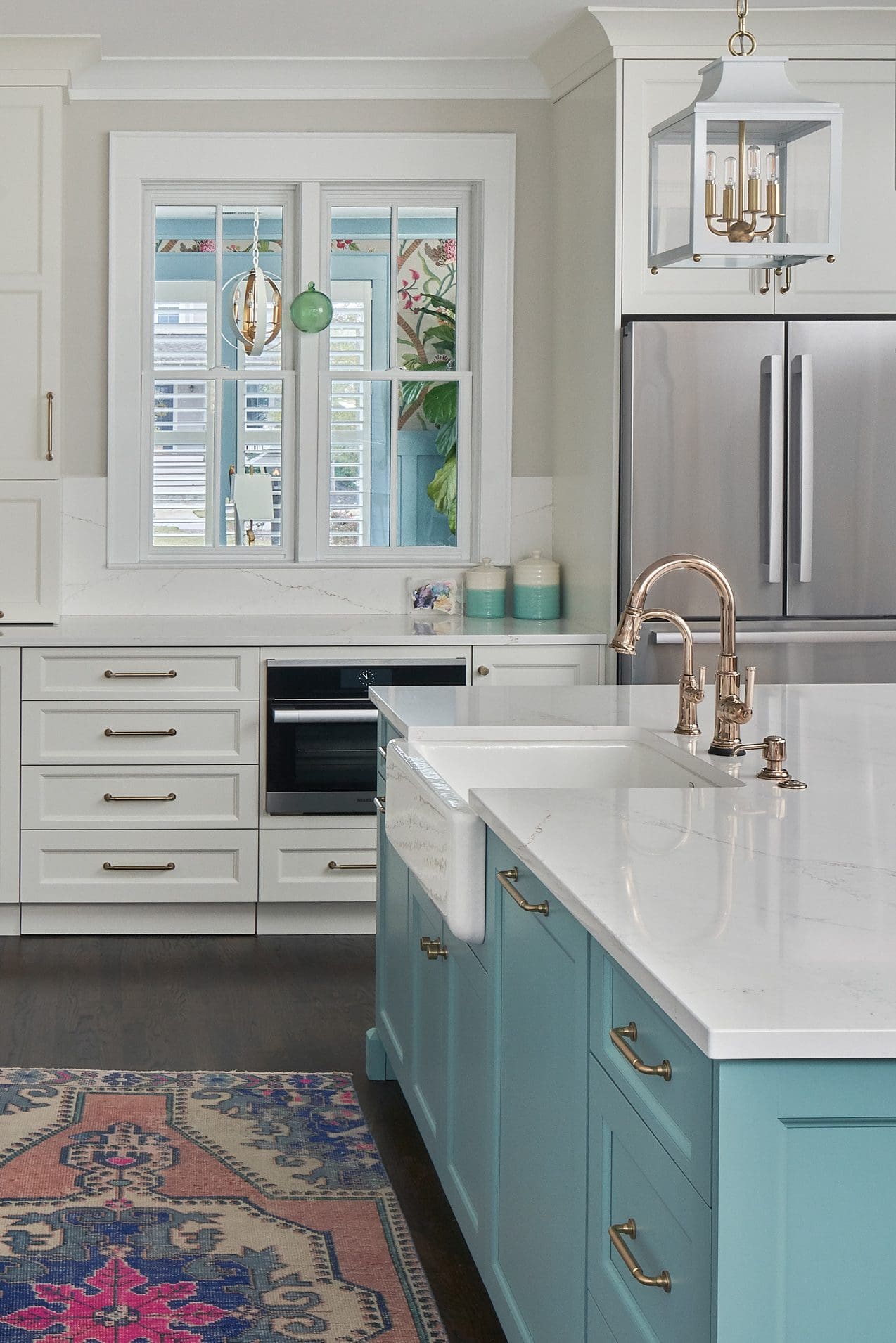 A kitchen with a cast iron farmhouse sink in a turquoise island with a gold faucet.