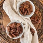 Two white bowls with candied pecans on a wooden bread board.