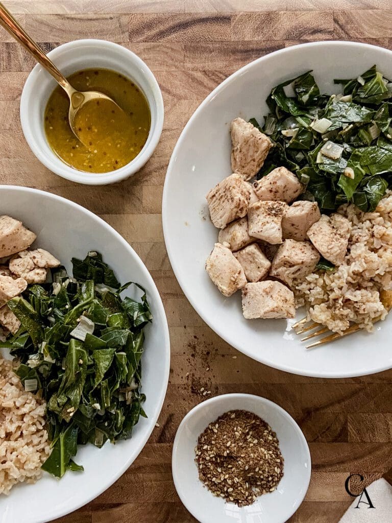 Two bowls of greens and chicken with an orange vinaigrette in a ramekin.