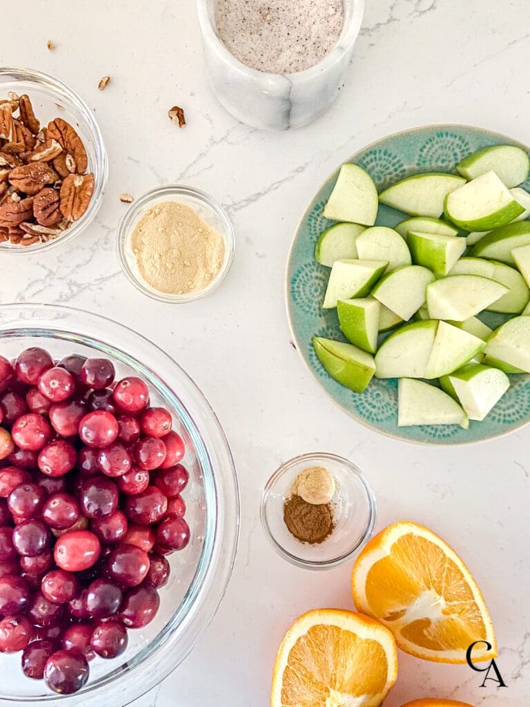 Cranberries, apple and orange slices in bowls on a counter with nuts and spices.