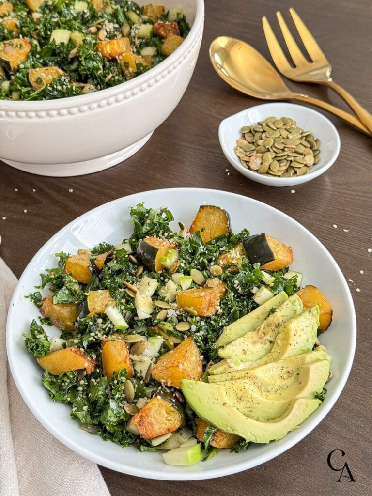 A bowl of kale apple salad with avocado slices and pumpkin seeds.