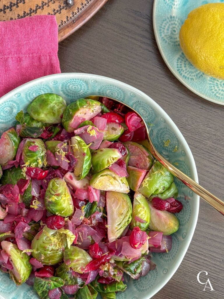 Brussels sprouts and cranberries in an aqua serving bowl with a gold spoon.