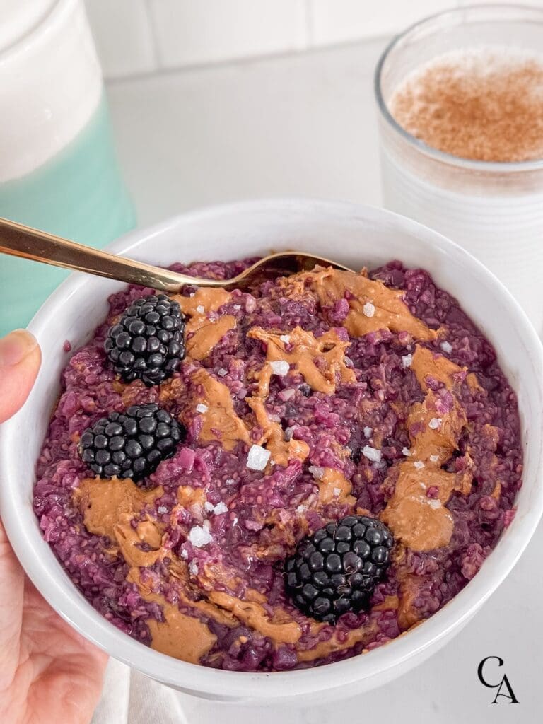 Steel-cut oats and peanut butter in a white bowl with blackberries and flaky salt.