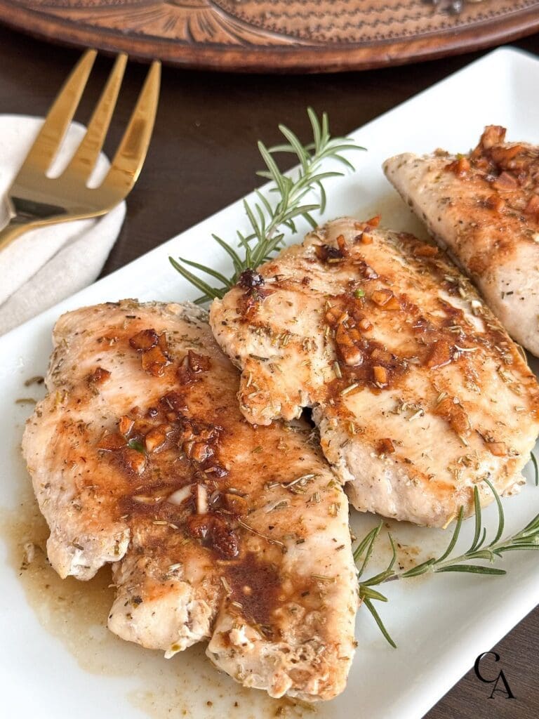 Cooked chicken breasts with rosemary sprigs on a plate.