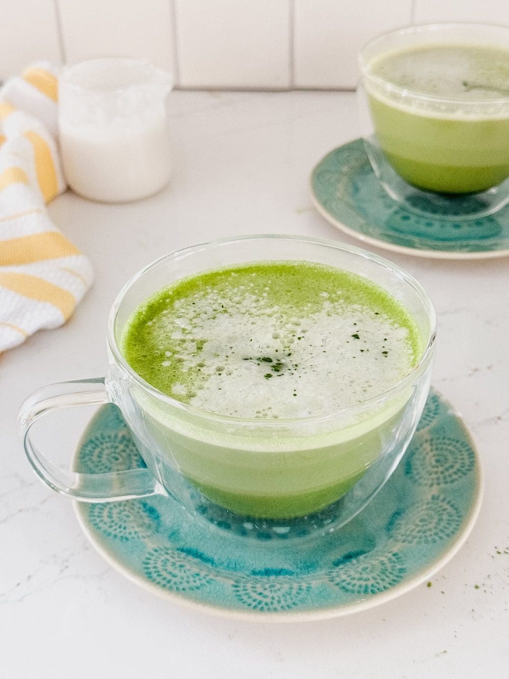 Two coconut milk matcha lattes on a white countertop.