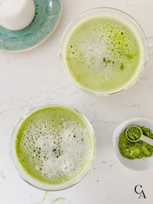 Two mint matcha lattes on a marble countertop.