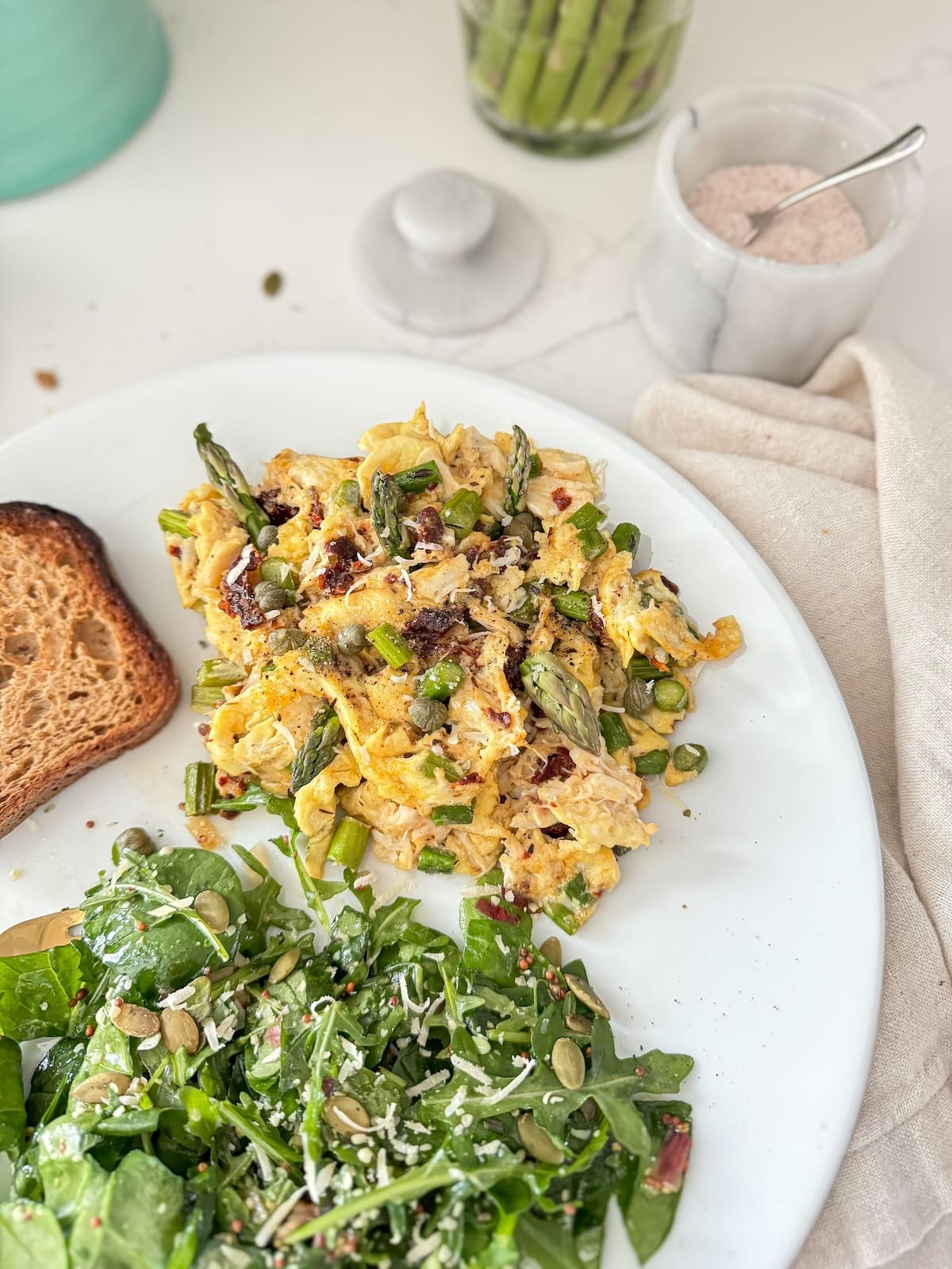A plate of scrambled eggs with crab meat and asparagus, next to a salad.