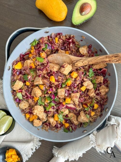 A large skillet of ginger chicken, mango slaw and cauliflower rice with a wooden spoon.