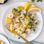 A plate of steamed cauliflower, yellow carrots and sautéed shrimp with parsley and lemon wedges.