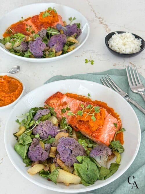 A bowl of steamed veggies and salmon with a linen napkin on a white countertop.