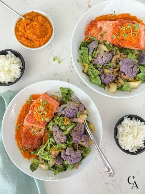 Seared salmon filets with colorful veggies in white bowls on a marble counter.