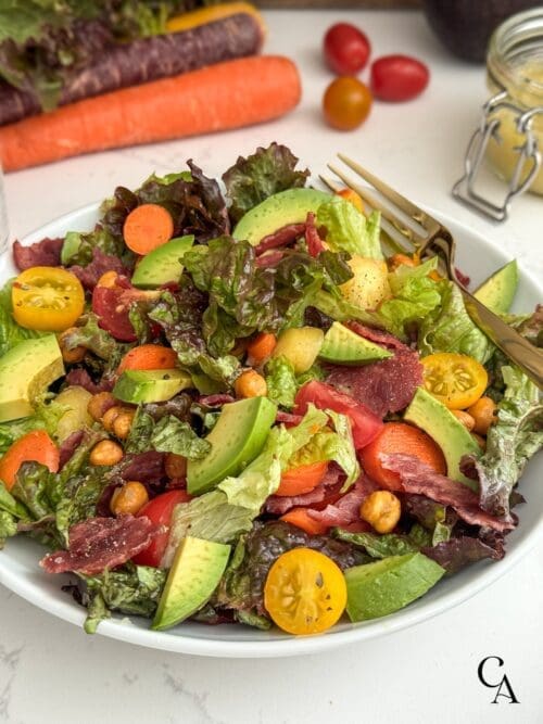 A salad with turkey bacon, lettuce, tomatoes, carrots, avocado and chickpeas.