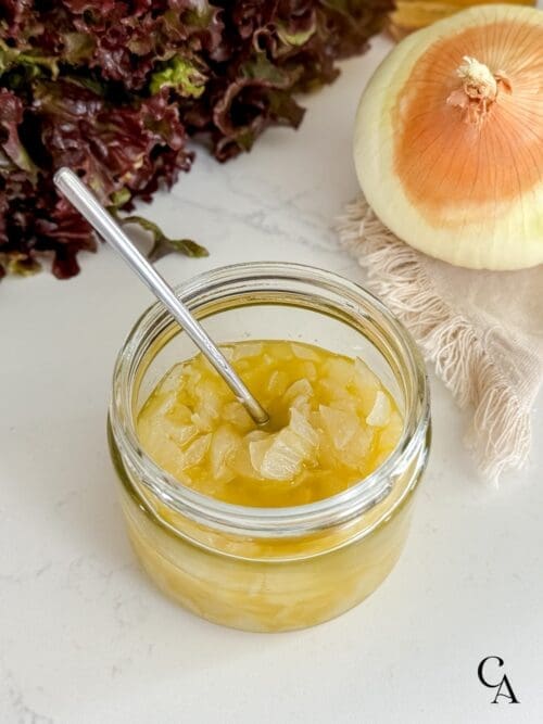 A glass jar of chunky sweet onion vinaigrette with an onion and red leaf lettuce.