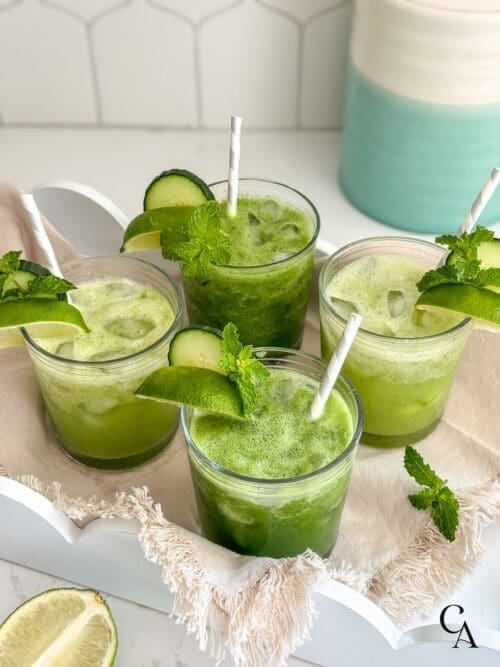 A tray of green drinks with cucumber, lime and mint garnishes.