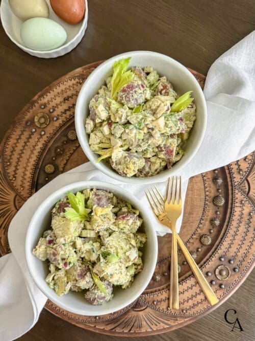 Two bowls of potato salad on a wooden board with a white linen napkin.