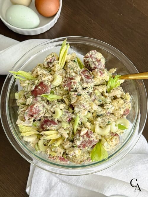 A glass bowl of potato salad with celery and eggs.