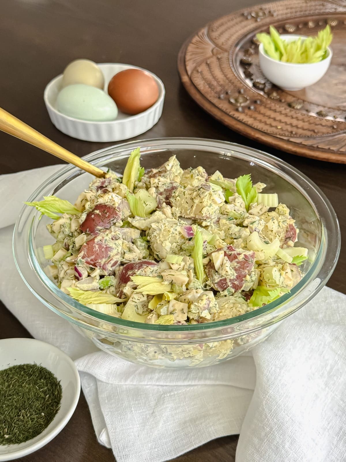 A bowl of chunky potato salad with eggs and celery leaves.