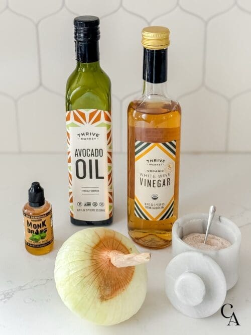 Bottles of oil and vinegar, a bowl of salt, and an onion on a white counter.