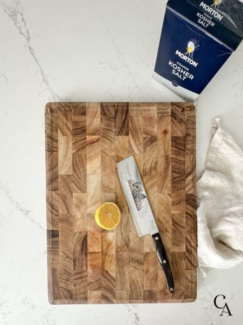 A cutting board with a chef knife and a sliced lemon.