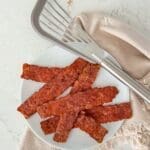 A plate of oven-baked turkey bacon next to a linen napkin.