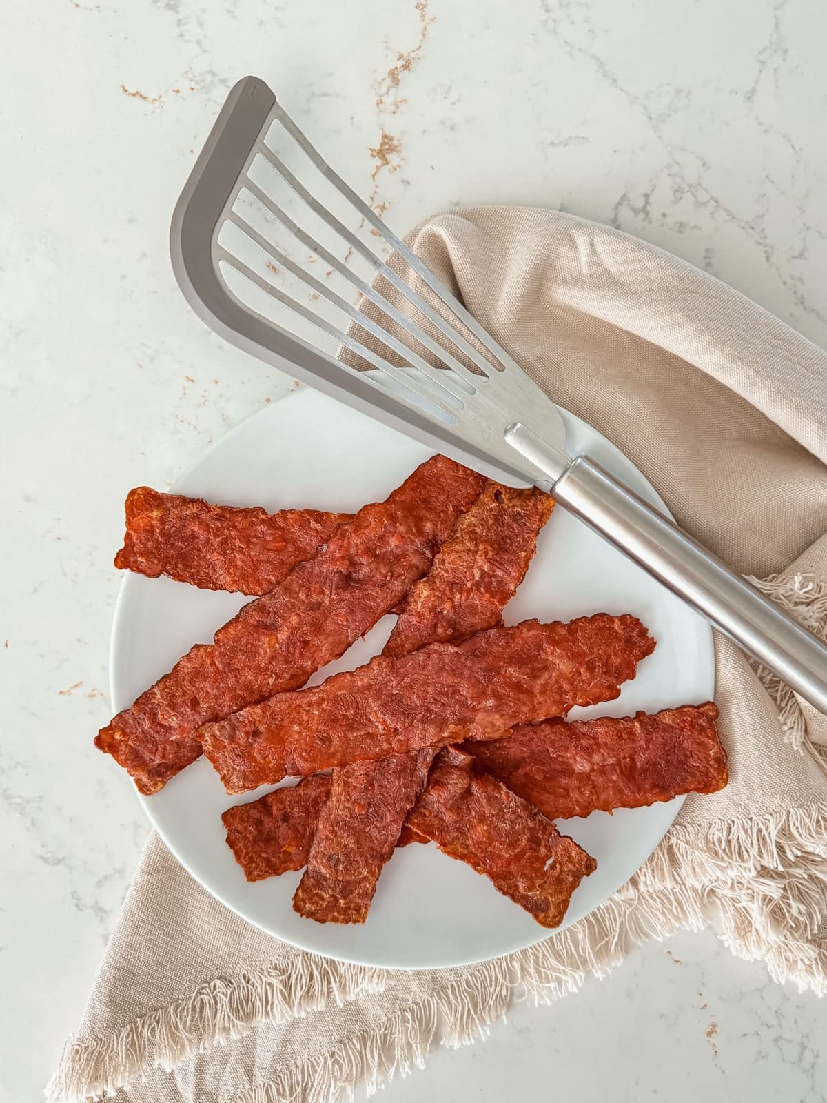 A plate of oven-baked turkey bacon next to a linen napkin.