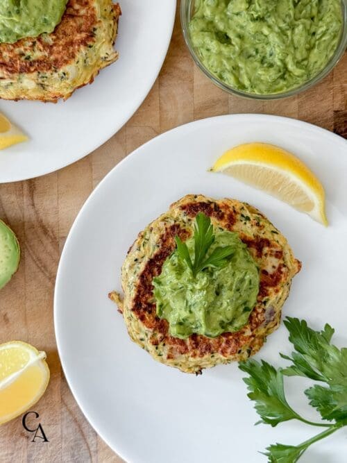 White plates with zucchini fritters, lemon and avocado.