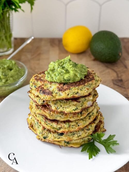 A stack of gluten-free zucchini fritters with avocado and parsley.