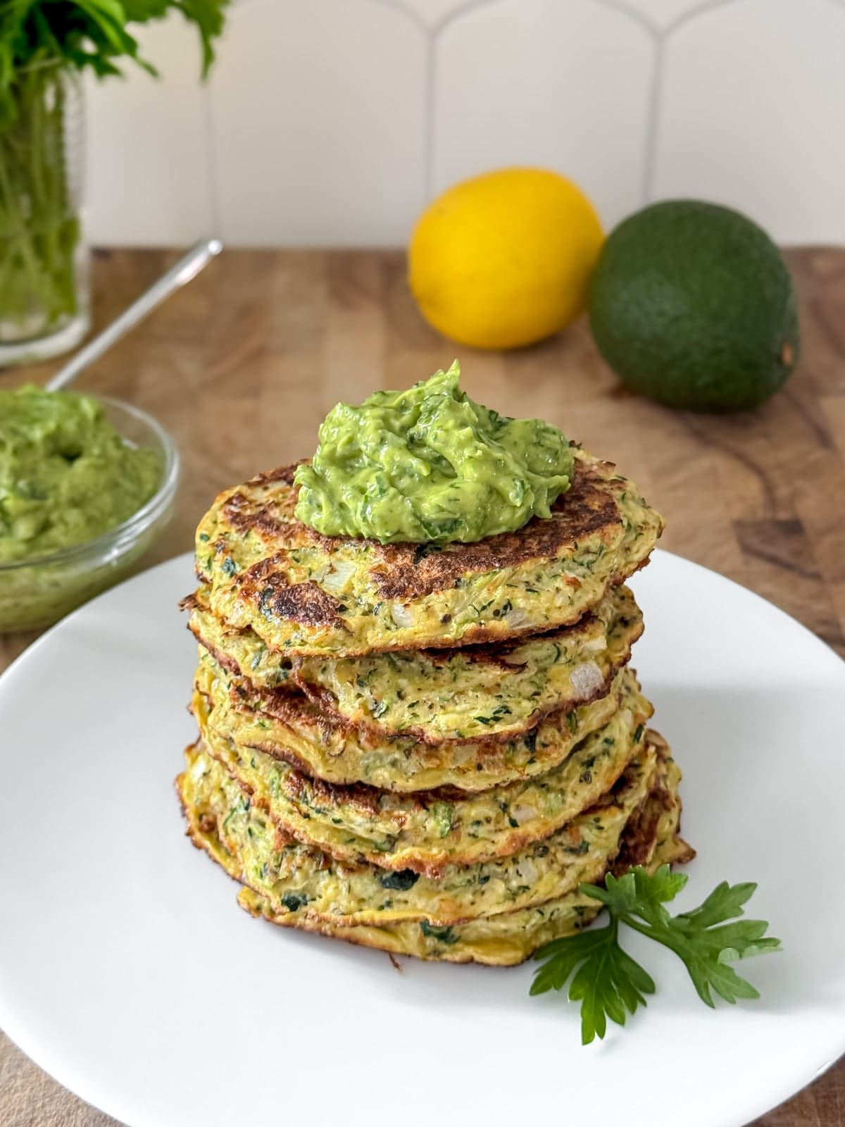 A stack of zucchini fritters with herbs and green sauce.