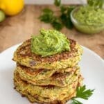 A stack of zucchini fritters on a white plate, topped with avocado gremolata.