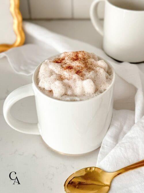 A cinnamon latte in a white mug, on a marble countertop.