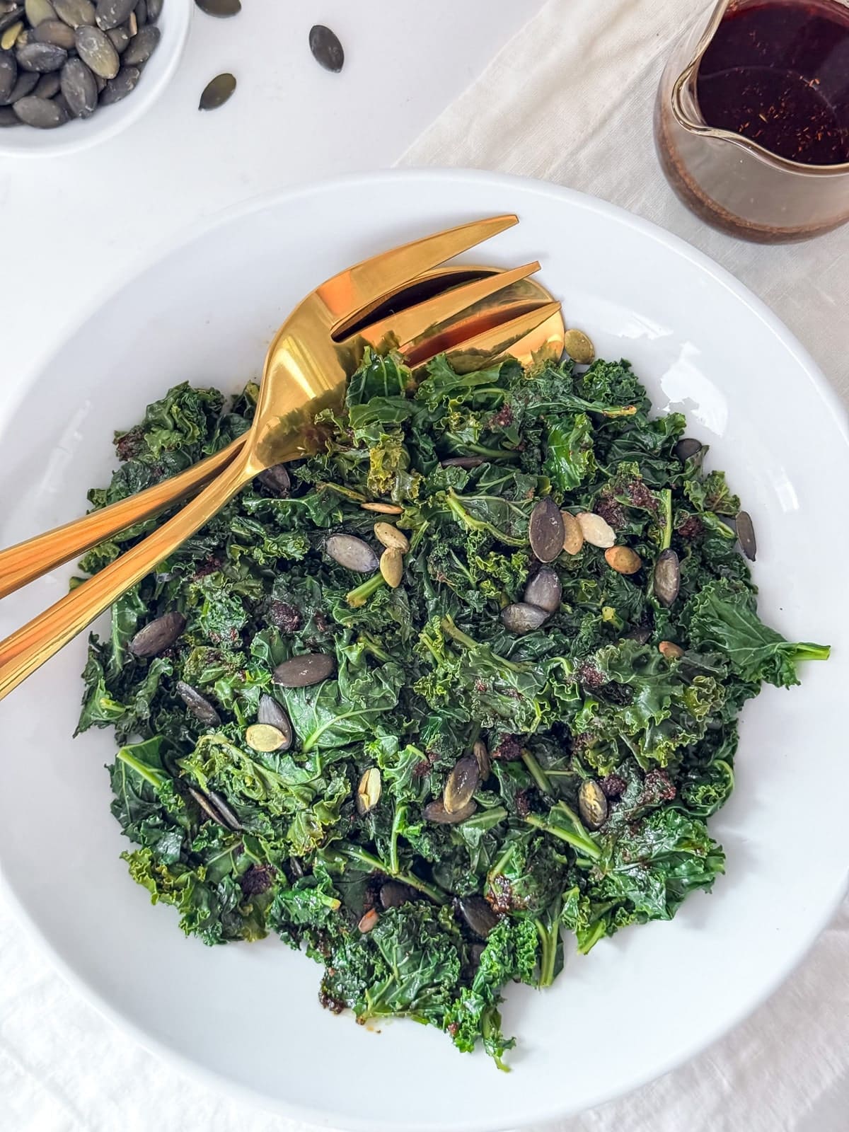 A bowl of kale with gold serving utensils.