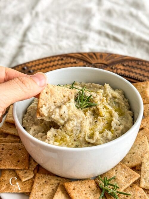 A hand scooping bean dip onto a cracker.