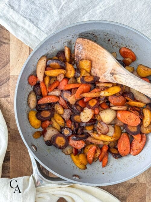 Sautéed rainbow carrots in a skillet with a wooden spoon.