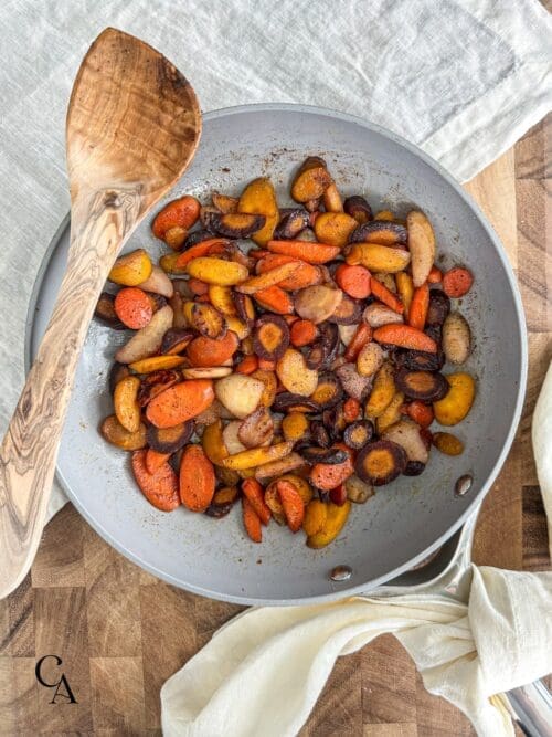 A pan of cooked carrots with a wooden spoon.