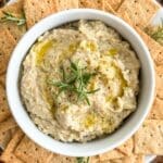 A bowl of white bean dip with rosemary.