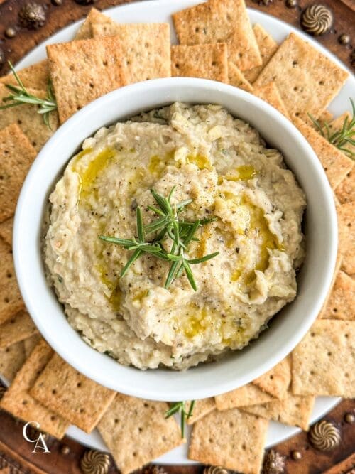 A bowl of white bean dip with rosemary.