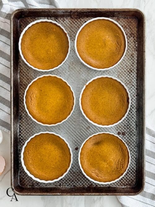 Six pumpkin custard cups on a rimmed baking sheet.