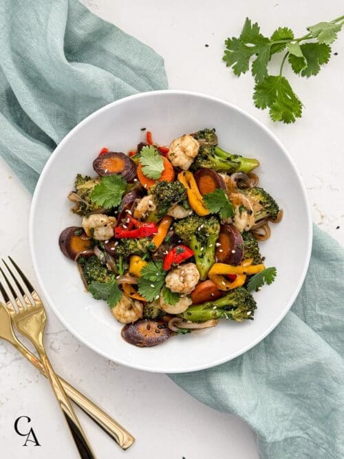 A bowl of shrimp stir fry with broccoli, peppers and carrots.