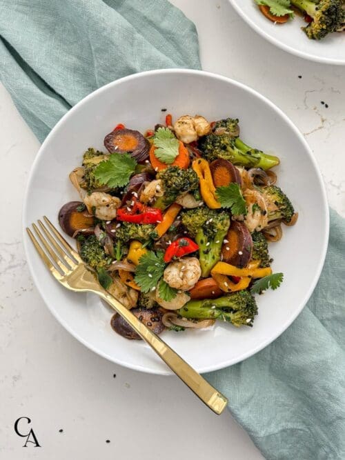 A bowl of cooked vegetables with shrimp and sesame seeds.