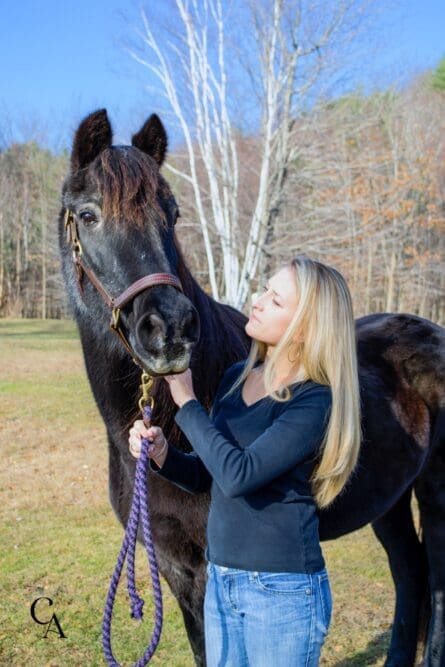 A young woman standing with a dark bay horse.