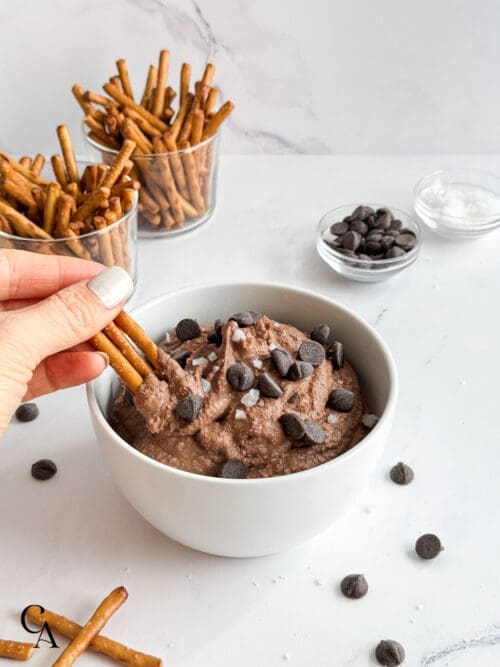 A woman dipping pretzel sticks into a bowl of chocolate hummus.