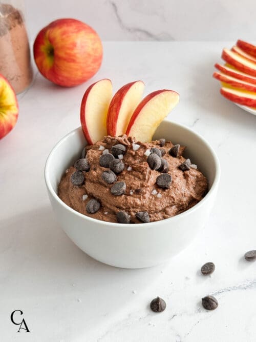 A bowl of dark chocolate hummus with sliced apples and chocolate chips.