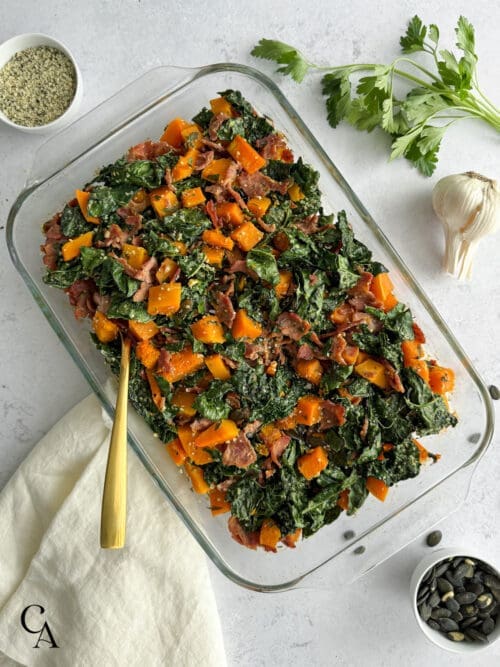 A butternut squash casserole in a glass dish with fresh parsley and pumpkin seeds.