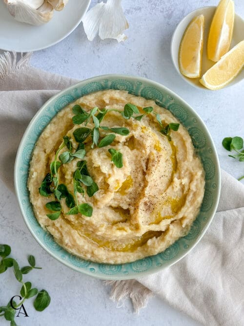 A bowl of celeriac purée with microgreens, garlic, and lemon wedges.