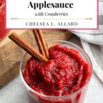 A bowl of red applesauce with cranberries and cinnamon sticks.