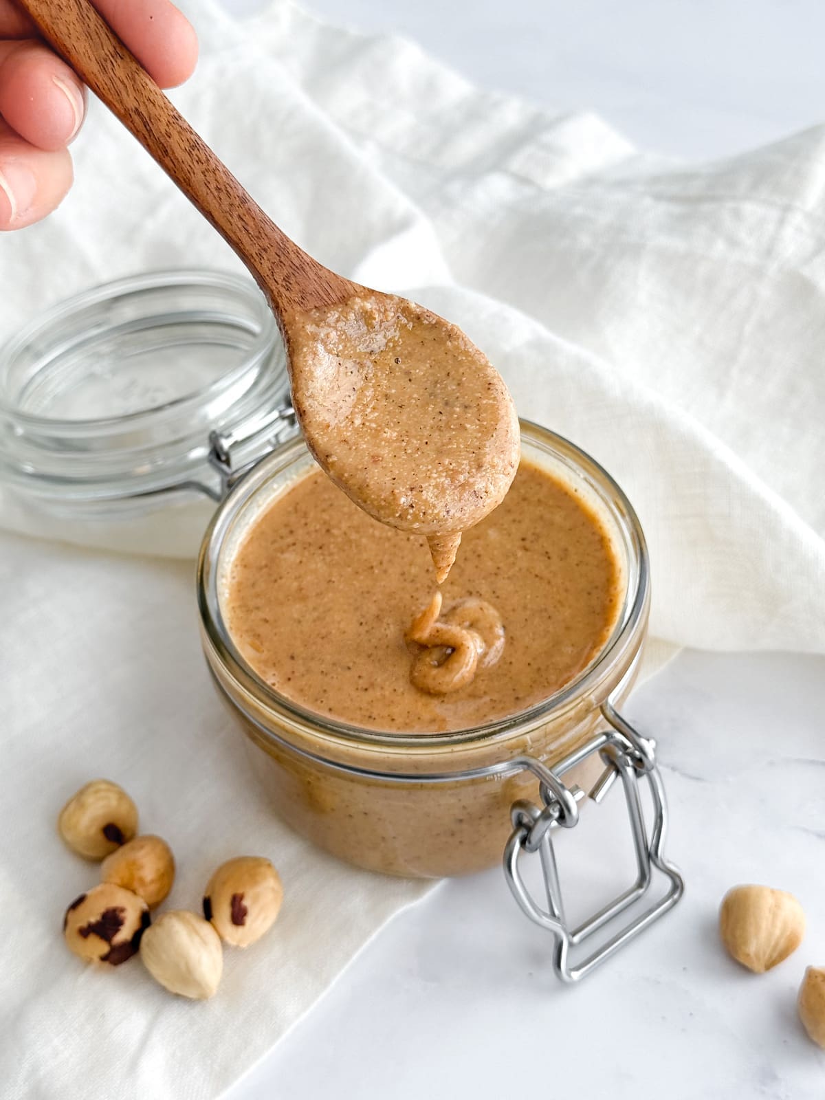 A jar of nut butter with hazelnuts on a white countertop.