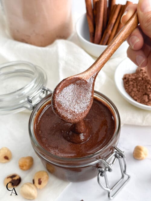 A spoonful of dark chocolate nut butter dripping over a glass jar.