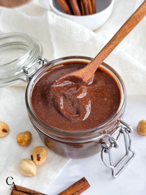 A jar of chocolate hazelnut butter with roasted nuts and cinnamon on a linen napkin.